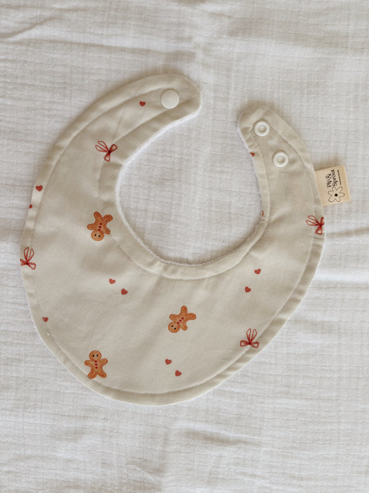Handmade Gingerbread Dreams Christmas Bib in beige with pink bows and hearts, made from organic cotton with bamboo terry backing. Perfect for baby’s first festive season.