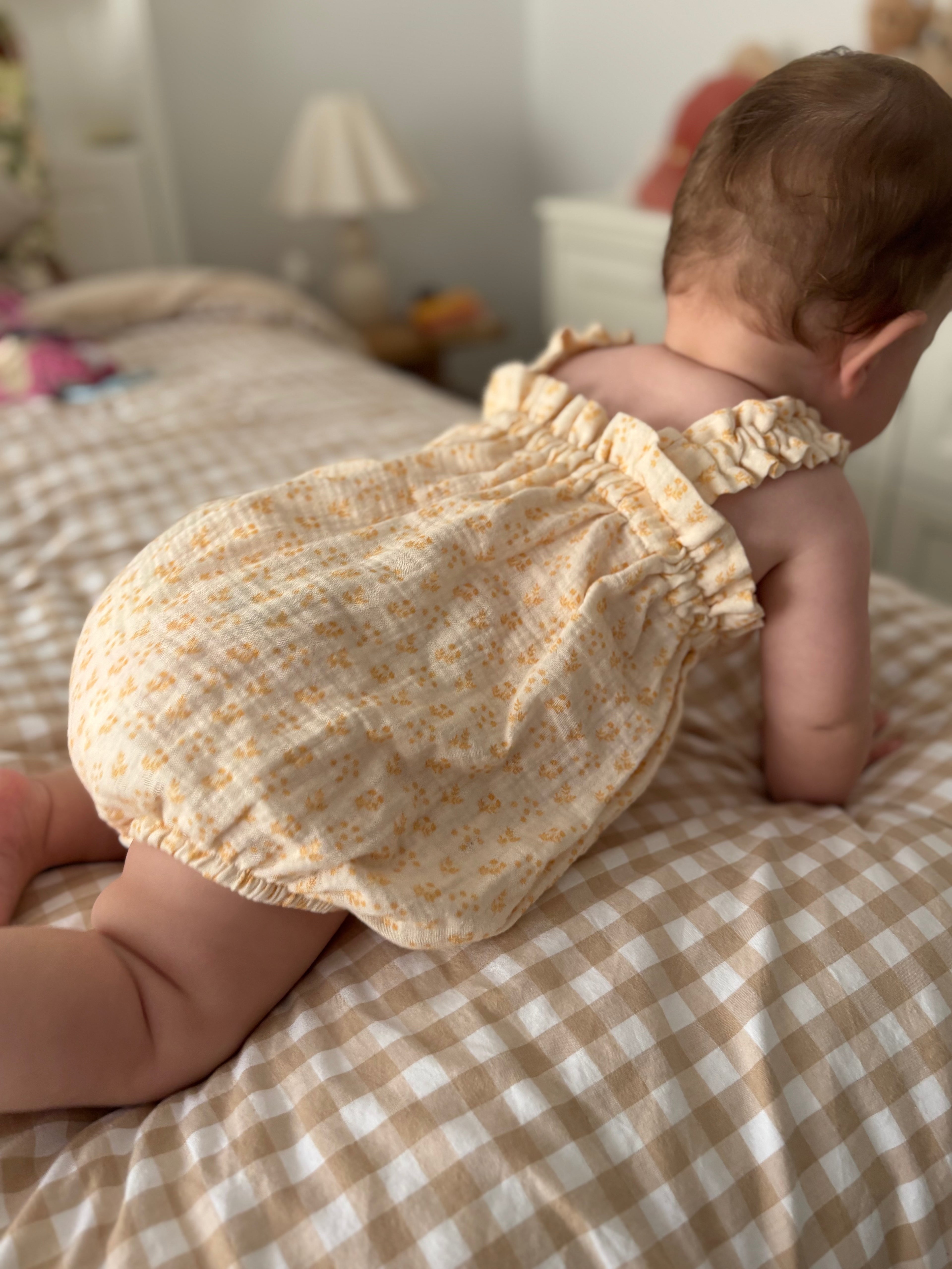 Baby in a floral romper sitting on a checkered bed